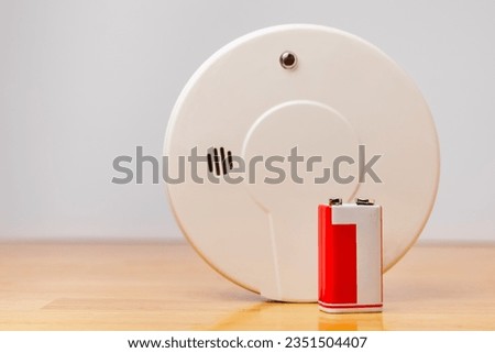 9v alkaline battery with home smoke detector background. Nine volt battery replacement for fire alarm safety.
