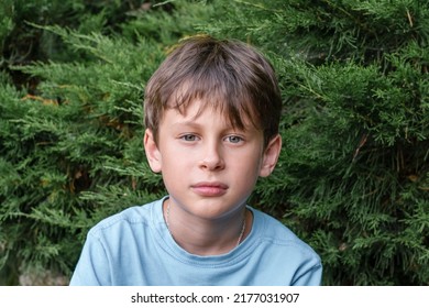 A 9-year-old Boy Looks Intently Into The Camera. Portrait Of A White Eastern European Boy In Nature