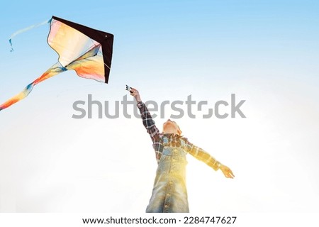 9YO Girl with flying colorful kite running on the high grass meadow in the mountain fields. Low angle camera view point. Happy childhood moments or outdoor time spending concept image. 