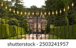 "A majestic 18th-century luxury mansion with classic British architecture from thw view of it boundary gate set amidst lush green grounds in the picturesque Cotswolds, 
