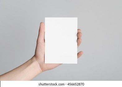 A6 Flyer / Postcard / Invitation Mock-Up - Male Hands Holding A Blank Flyer On A Gray Background.