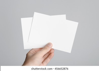 A6 Flyer / Postcard / Invitation Mock-Up - Male hands holding blank flyers on a gray background.