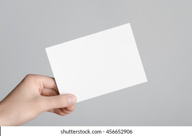 A6 Flyer / Postcard / Invitation Mock-Up - Male Hands Holding A Blank Flyer On A Gray Background.