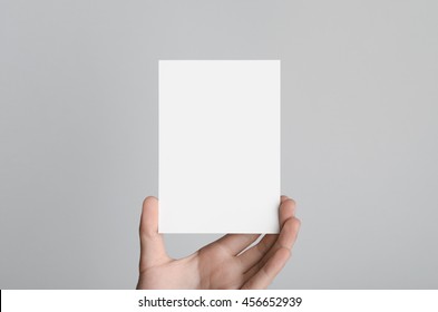 A6 Flyer / Postcard / Invitation Mock-Up - Male Hands Holding A Blank Flyer On A Gray Background.