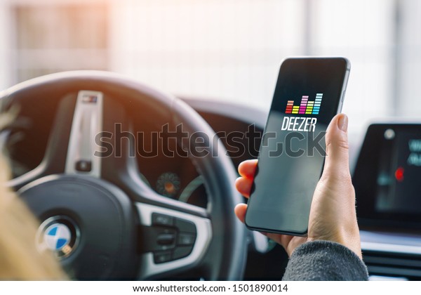 AACHEN, GERMANY AUGUST 2019: Woman holding a Apple\
iPhone opening Deezer Music streaming app in a car. Streaming music\
via the Internet 