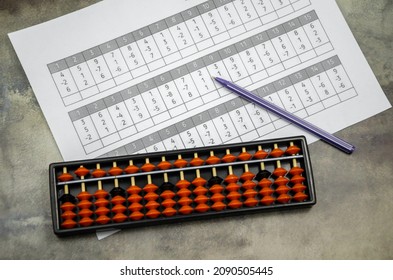 Abacus For Mental Arithmetic On The Background Of A Sheet Of Paper With Examples For Calculation. Accessories For Mental Arithmetic. Abacus, Pen And Sheet Of Paper On The Desktop