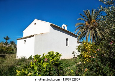 Abadoned church Ermita de Sant Antoni y Sant Jaume between palm tree and green plants with cloudless blue sky in Cap Blanche , Altea, Spain