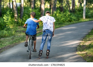 ABAKAN, RUSSIA - JULY 22, 2020: Two boy friends riding a bicycle and roller skating in a park in summer morning. - Shutterstock ID 1781594825