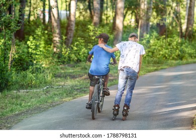Abakan, Russia - July 22, 2020: Two boy friends riding a bicycle and roller skating in a park in summer morning. - Shutterstock ID 1788798131