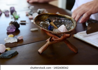 Abalone Shell with Palo Santo, and filled with healing crystals. Rose Quartz, Smokey Quartz, Sodalite, and Clear Quartz.  Burning palo santo in a abalone shell, being held. Variety of crystals shell