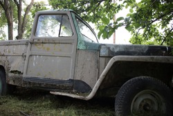 An Abandoned Antique Classic Vintage Pickup Truck, As It Looks From The Side. It Has Faded Colour And Little Somehow Opened Door, With Broken Window, Under A Tree, Kozani, Macedonia, Greece.