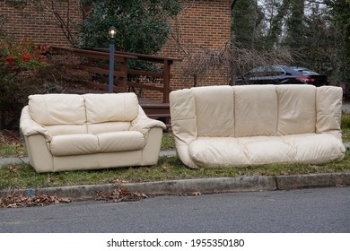 Abandoned Beige Couches On The Grass By A Curb In Front Of A House Waiting To Be Removed On Trash Day