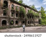 Abandoned building in Akarmara town, Tkvarcheli city, Abkhazia. Lone person looks at old ruins overgrown by grass and ivy in summer. Concept of war, grunge, architecture, nature, landmark.