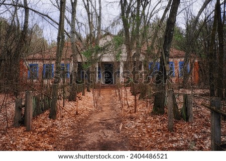 An abandoned building in a state of disrepair in a wooded area. The facade of an abandoned kindergarten in the Chernobyl radioactive zone. Autumn foliage on the ground. Trees in front of an old house.