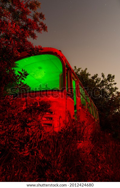 abandoned\
bus illuminated with colored lights at\
night
