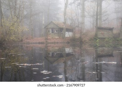 Abandoned cabin next to a small wooden shed with reflections in the water of a lake in the Palatinate forest of Germany on a foggy fall day. - Powered by Shutterstock