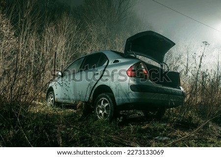 Abandoned car with open trunk in countryside, deserted auto, night scenery. Dangerous area, misty landscape
