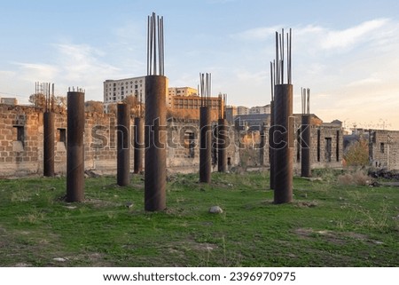 Abandoned construction site. Columns with protruding reinforcement. Construction of house is temporarily frozen. Construction site overgrown with grass. Abandoned walls from unfinished building