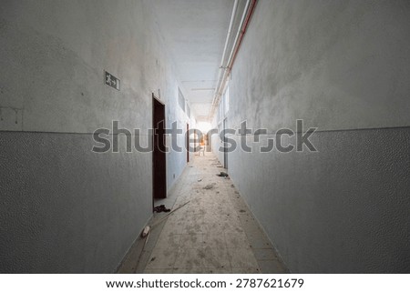 Abandoned Corridor with Emergency Exit Sign and Debris Leading Through Decaying Institutional Interior