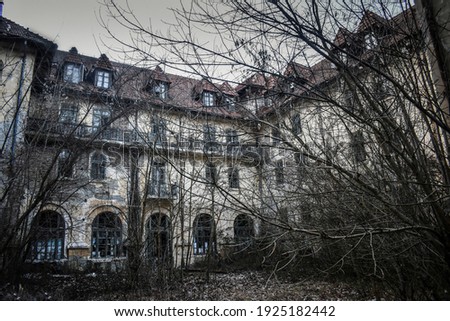 Abandoned creepy looking tall old trees without leaves in front of old abandoned hotel building. Creepy haunted hotel with dark horror atmosphere and spooky details. 
Scary view of ancient mansion.