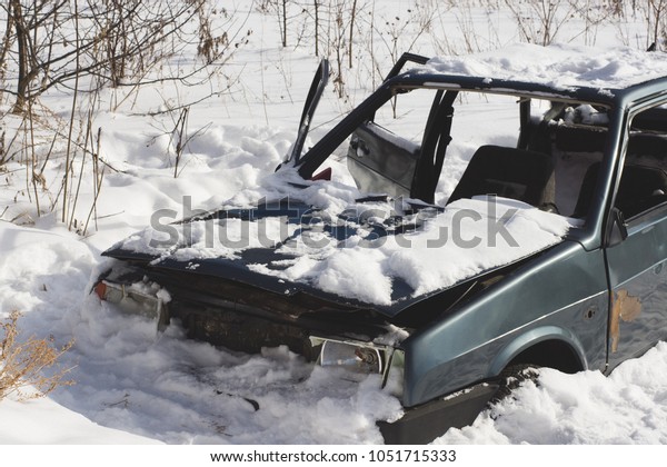 Abandoned destroyed car in the snow.\
Skeleton of unnecessary transport with broken\
headlights