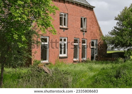 An abandoned and dilapidated farm house with red bricks and broken glass on a neglected terrain with tall grass. Concept of rural depopulation.