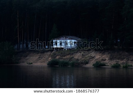 abandoned dilapidated house on a dark wooded bank is ready to collapse into the river