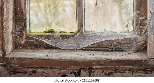 Abandoned, Dirty And Dusty Window Covered In Spiderwebs In Empty House From Poverty And Economic Crisis. Old, Damaged And Weathered Wooden Windowsill And Wood Frame Rotting From Dampness And Neglect