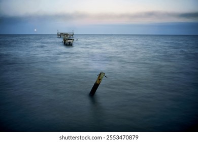 An abandoned dock extends into the tranquil sea - Powered by Shutterstock