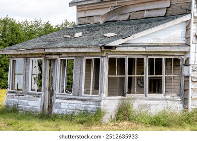 Abandoned empty deserted house home. Derelict disrepair torn siding missing shingles broken windows window frames. Enclosed front porch. Country rural property. Forlorn sad. Weathered distressed. - Powered by Shutterstock