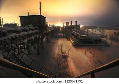 Abandoned Factory, In Winter, With Barrels And Pipes On The Horizon Glowing Lights Industrial Areas, Night Landscape