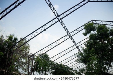 Abandoned greenhouse warehouse metal structure frame roof cover with tree and plant overgrown against blue sky in spring summer daytime - Powered by Shutterstock