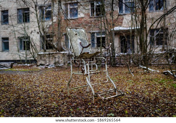 Abandoned gynecological\
chair against the background of a hospital building in the\
abandoned city of\
pripyat