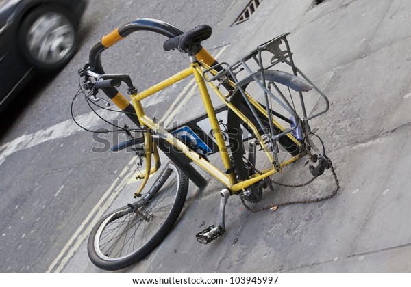 Abandoned and heavily damaged bicycle locked at\
parking lot