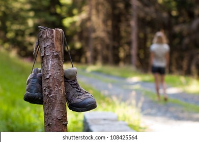 Abandoned hiking shoes with a woman walking bare feet