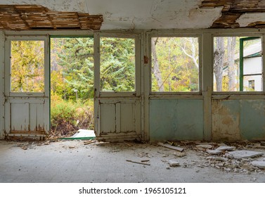 Abandoned House Interior. Gallery With Door And Window Frames, Broken Glass And Fallen Plaster, Overgrown Autumn Garden Seen Through The Windows