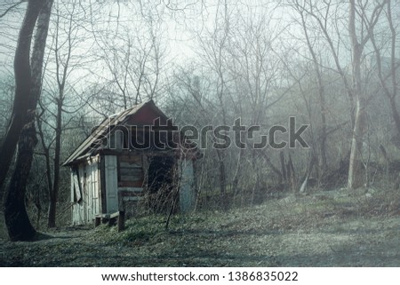 Abandoned hunting lodge in autumn forest. Dilapidated old wooden hut ruins in foggy wood, spooky landscape