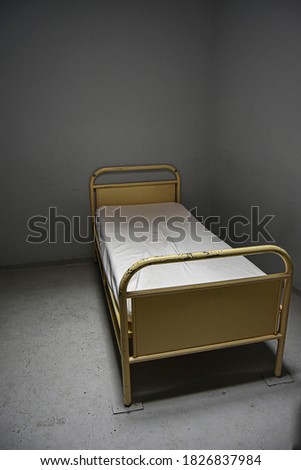 abandoned isolation cell in a hospital, hot topic in psychiatry, punishment, lonely cell, grey background with bed nailed to the ground. Lonely isolation, small cells, back to basic, great picture