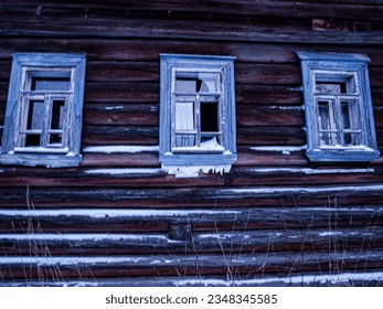An abandoned log cabin with broken windows. Frosted in winter. The abandonment of the hinterland, alienation, decline.