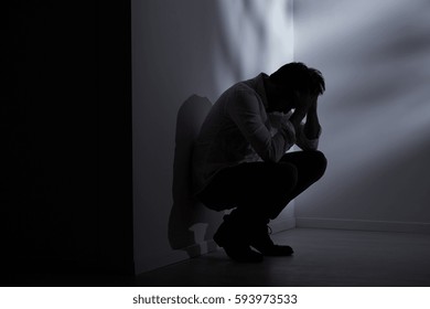 Abandoned and lost man sitting beside wall in dark room