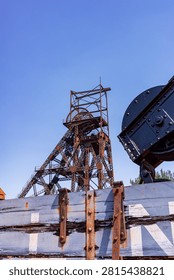 Abandoned mining headframe and rusty winding gear rise under a clear blue sky, symbolizing obsolescence, industrial heritage, and the decline of the coal industry