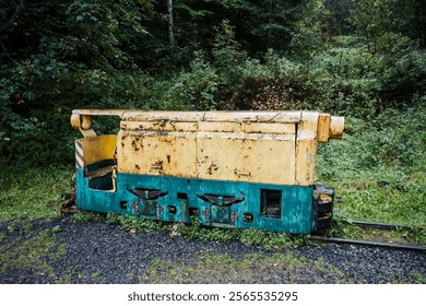 An abandoned mining locomotive sits peacefully among overgrown vegetation, showcasing its weathered body and colorful paint. This relic of industry contrasts with the surrounding forest. - Powered by Shutterstock