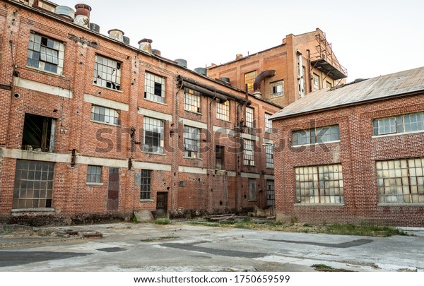 Abandoned multi-story red brick factory building\
with broken glass\
windows.