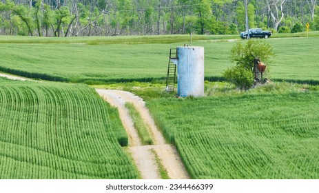 Abandoned oil pump jack next to tank with maintenance road in middle of farm field aerial - Powered by Shutterstock