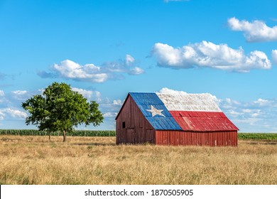 An abandoned old barn with the symbol of Texas painted on the roof sits in a rural area of the state, framed by farmland.
