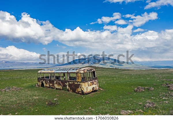 Abandoned old bus in a field of Armenia with a mountain\
in background 