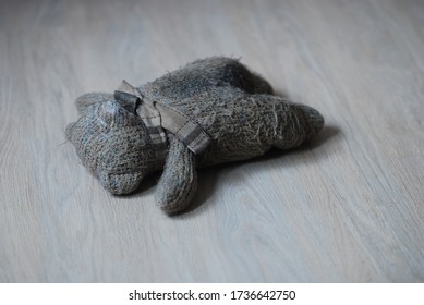 Abandoned Old Dirty Brown Wool Toy Bear On Which A Brown Scarf Is Tied, Lies On A Light Wooden Floor. Isolated