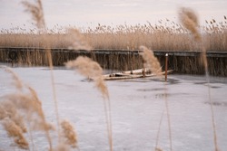 An Abandoned Old Rowboat Sinking In The Icy Lake Amidst The Reeds.