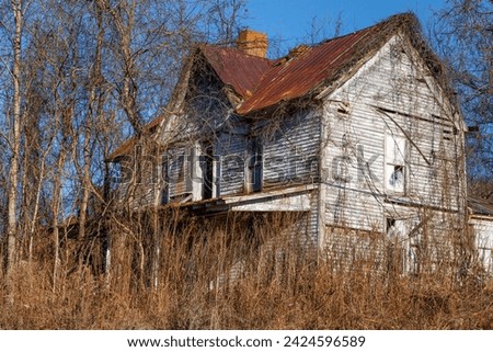 Abandoned olf farm house decaying and overgrown with plant vines in rural Tennessee.