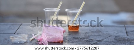 Abandoned plastic cups with straws and plastic wrapper left on outdoor stone surface representing single use plastic waste and urban littering problem
